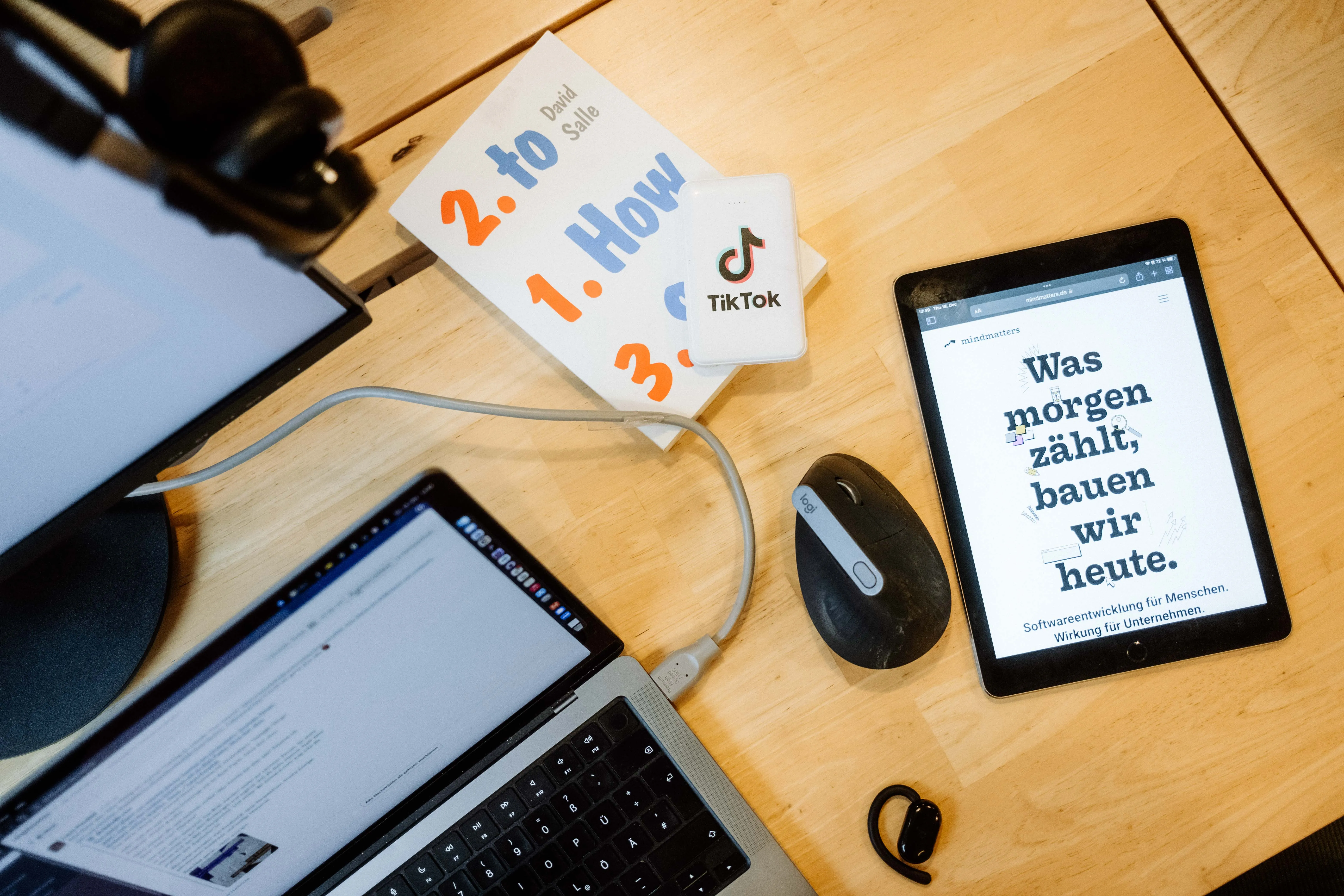 Schreibtisch von oben mit Laptop, Tablet und Notizen aus dem Arbeitsalltag.