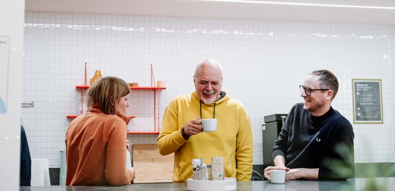Drei Personen im Gespräch bei einer Tasse Kaffee in der Büroküche.